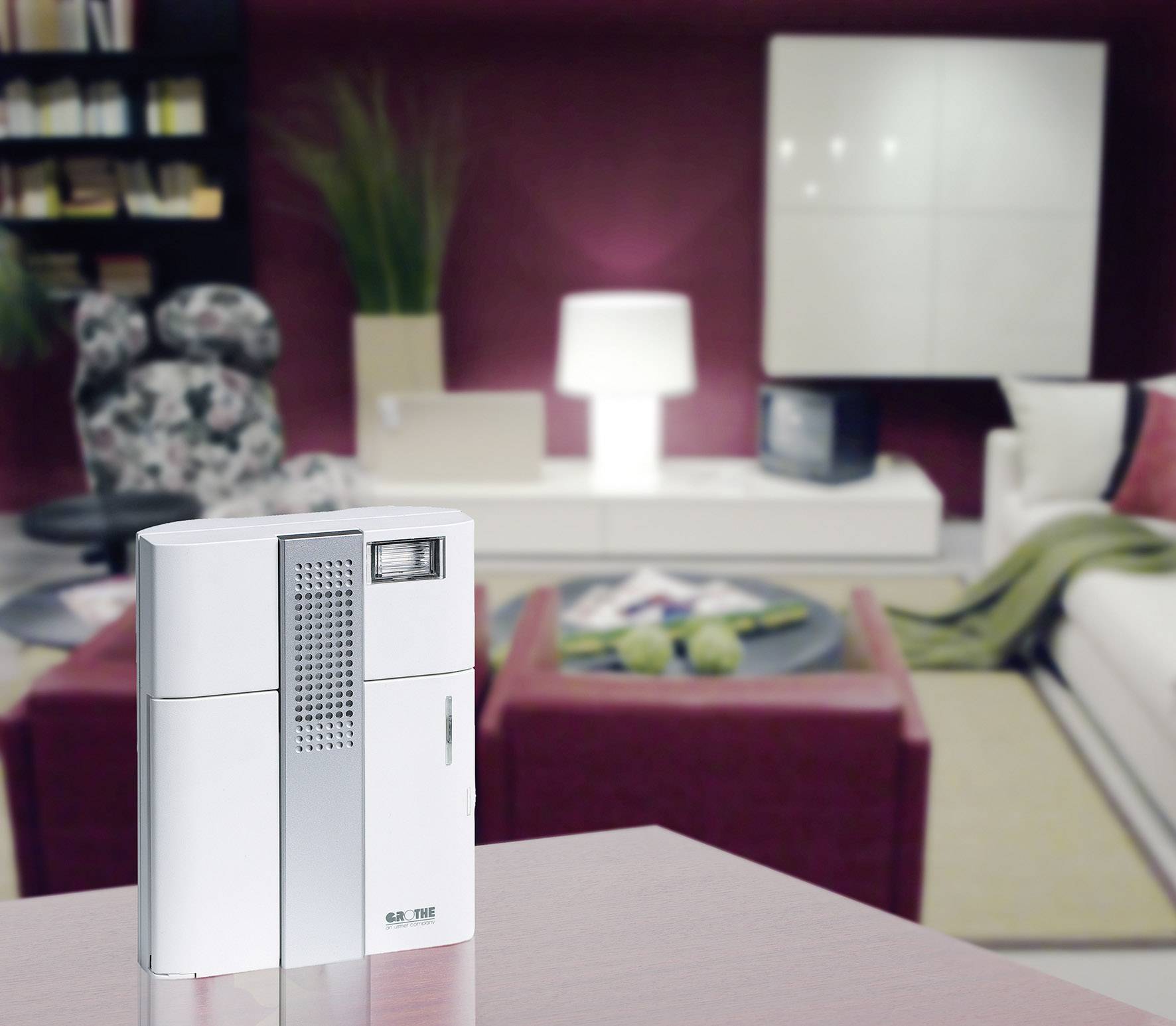 A white air purifier is sitting on a table in a modern, stylishly furnished living room. Furniture and decorations can be seen in the background.