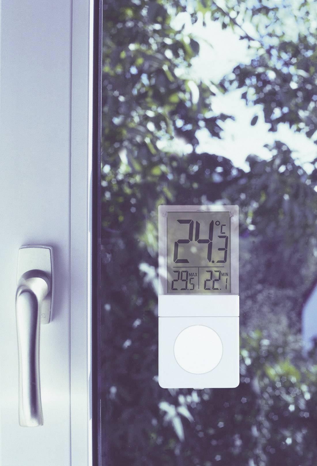 A thermometer shows 24°C on a sunny day. It is mounted on a window through which green trees can be seen.
