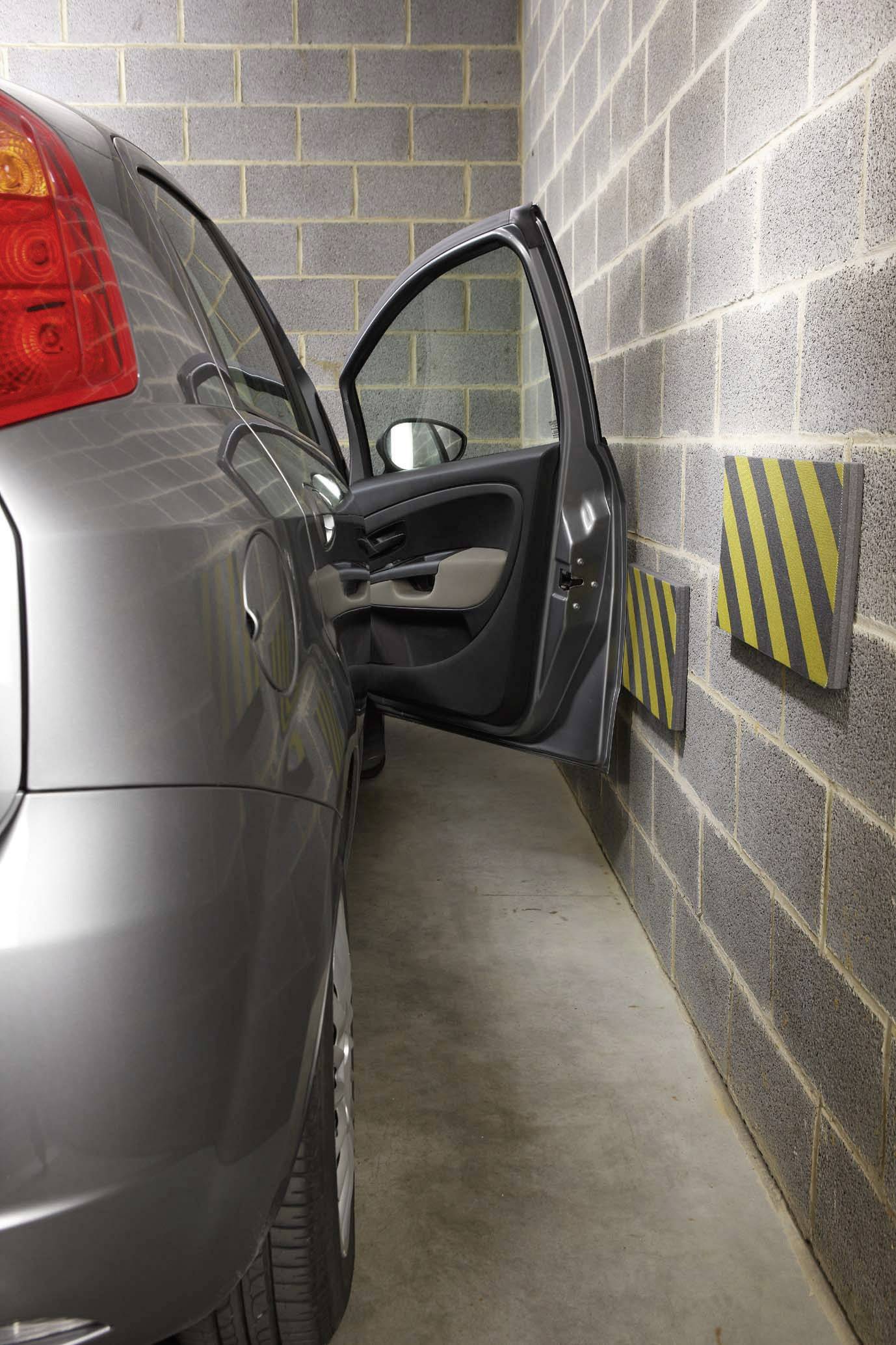 Silver car parked in a narrow garage, driver's door open, yellow and black protective padding on the wall to prevent paintwork damage.