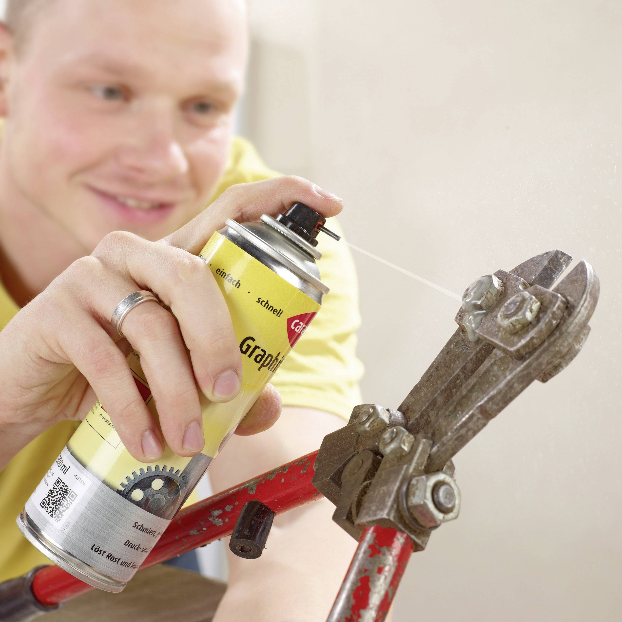 A person is using a yellow-black metal care spray with graphite to lubricate a tool or piece of metal.
