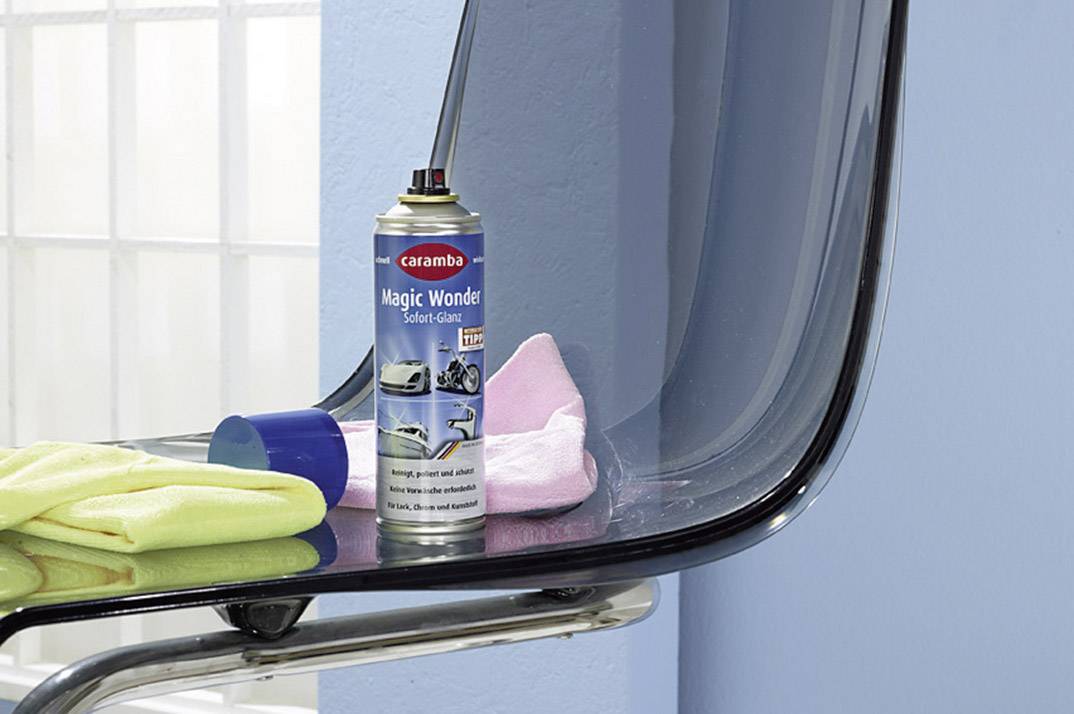 A spray can 'Magic Wonder', surrounded by cloths of various colours, sits on a transparent chair in front of a blue wall.