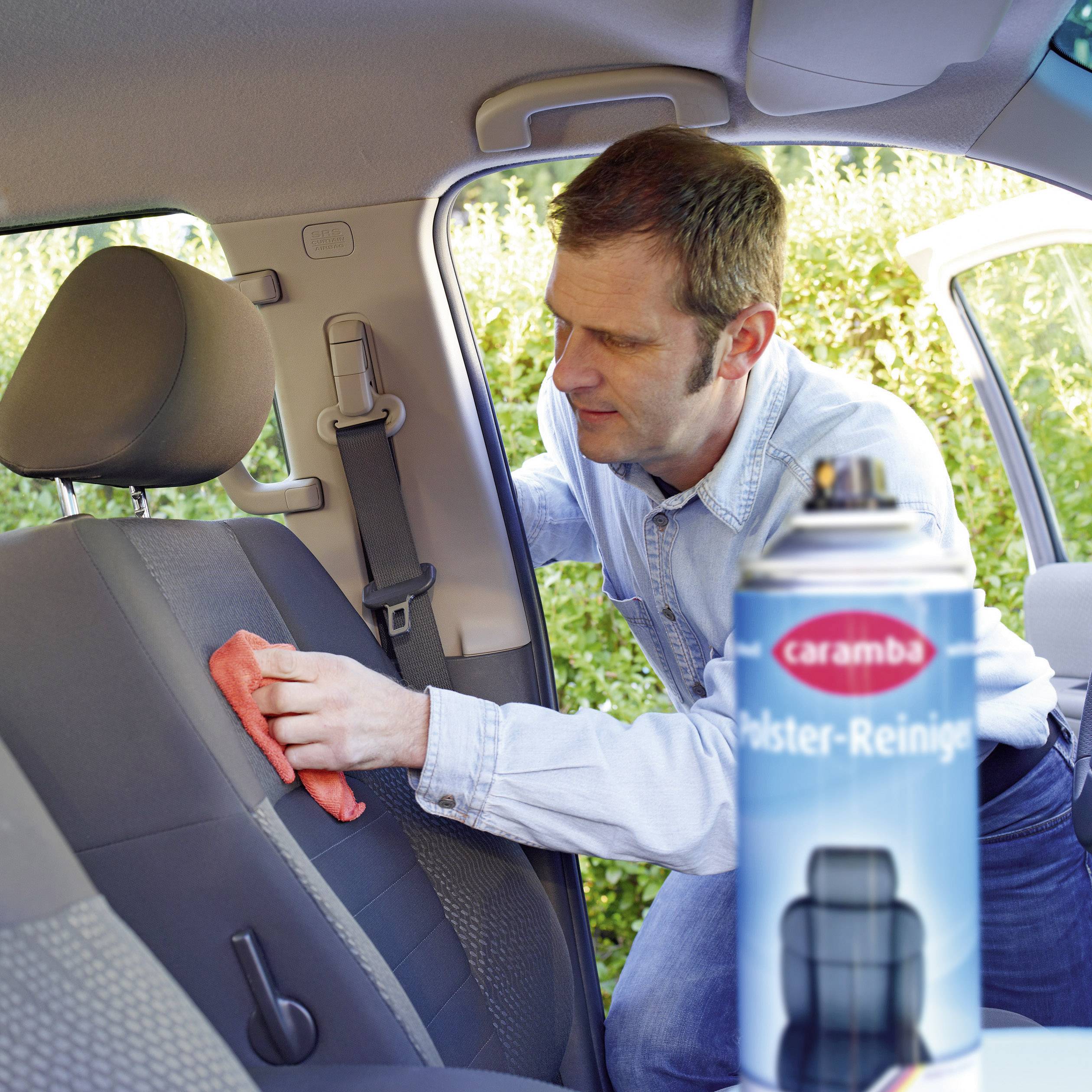 A person is cleaning the back seat of a car with a cloth and a cleaning product. A label on the cleaner shows 'Caramba'.