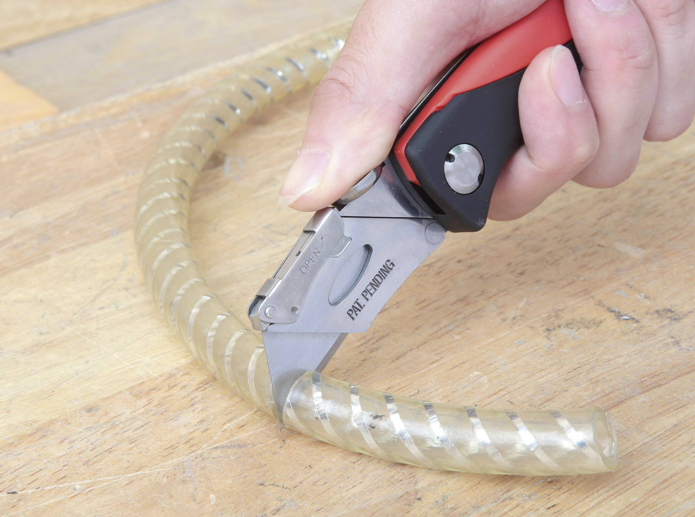A person is cutting a transparent tube with a utility knife on a wooden table.