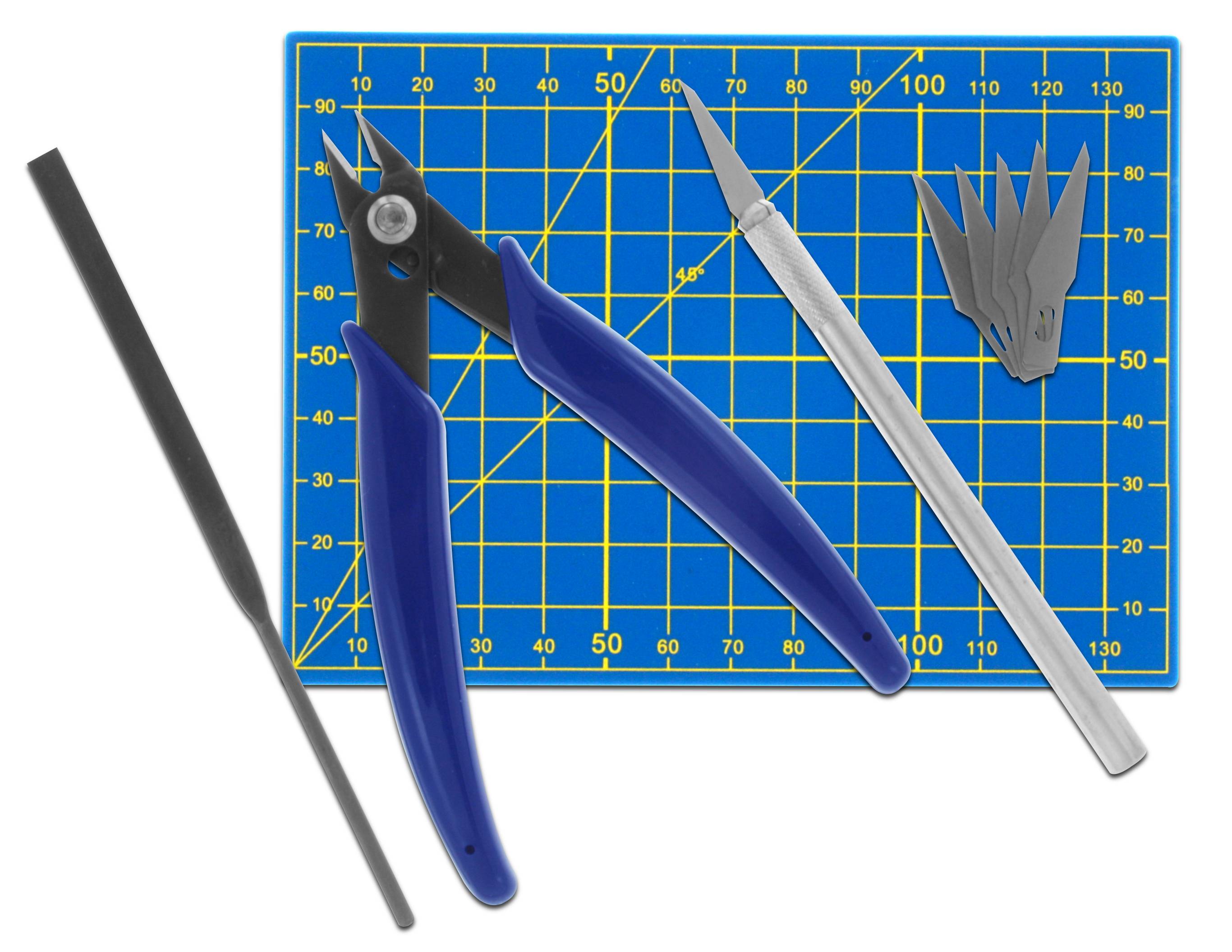 Cutting tools and blades on a blue cutting mat with a yellow grid pattern. On the left, a file; in the centre, pliers; on the right, a craft scalpel and blades.