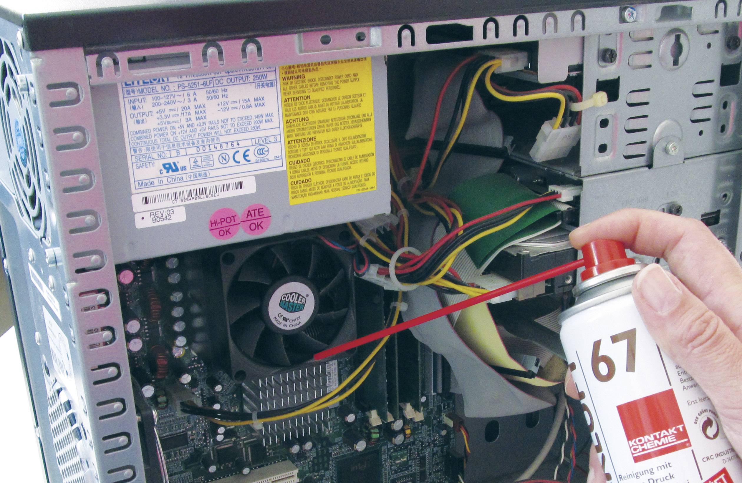 Open computer with casing, built-in fan and wiring. A hand sprays compressed air from a can to remove dust.