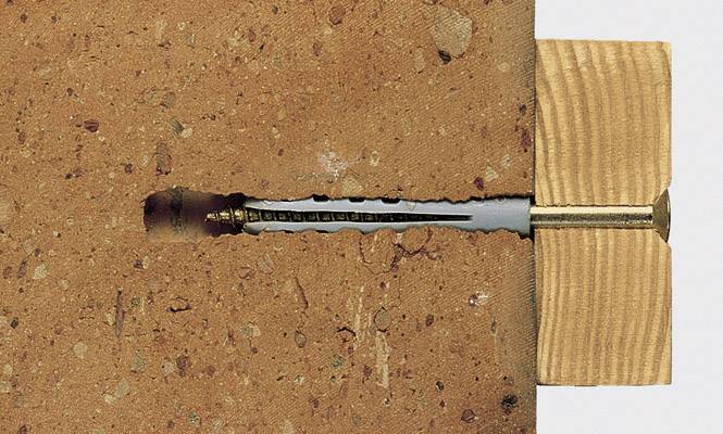 A wall plug is anchored in a brick, supporting a piece of wood above it. Demonstrates the principle of anchoring.