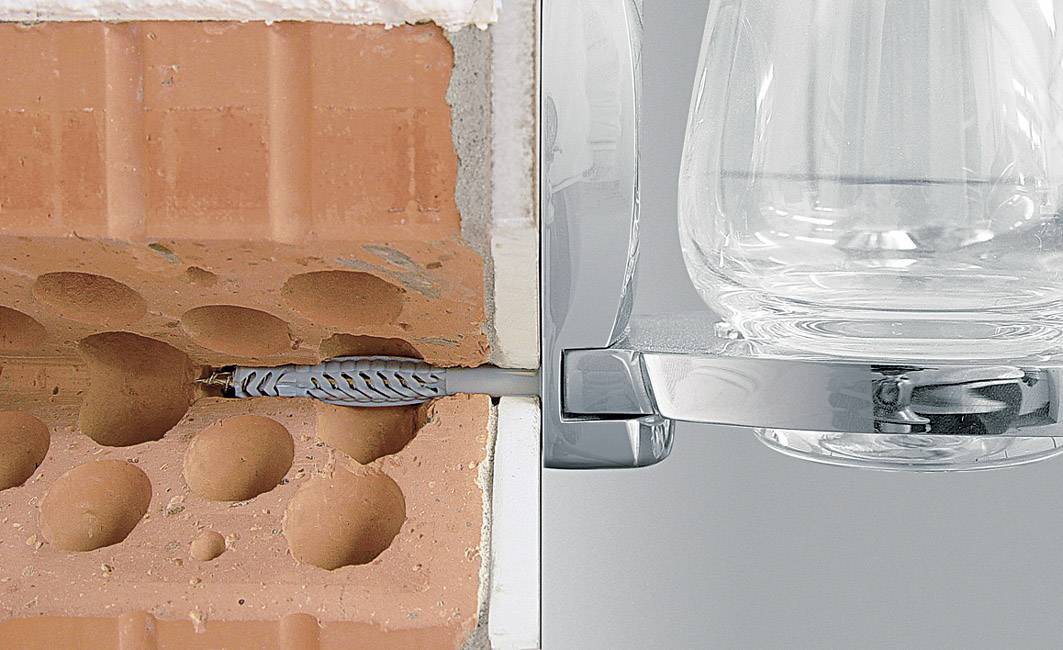 A brick wall in red on the left, with a cable recessed into the wall. On the right, part of a transparent glass carafe is visible.