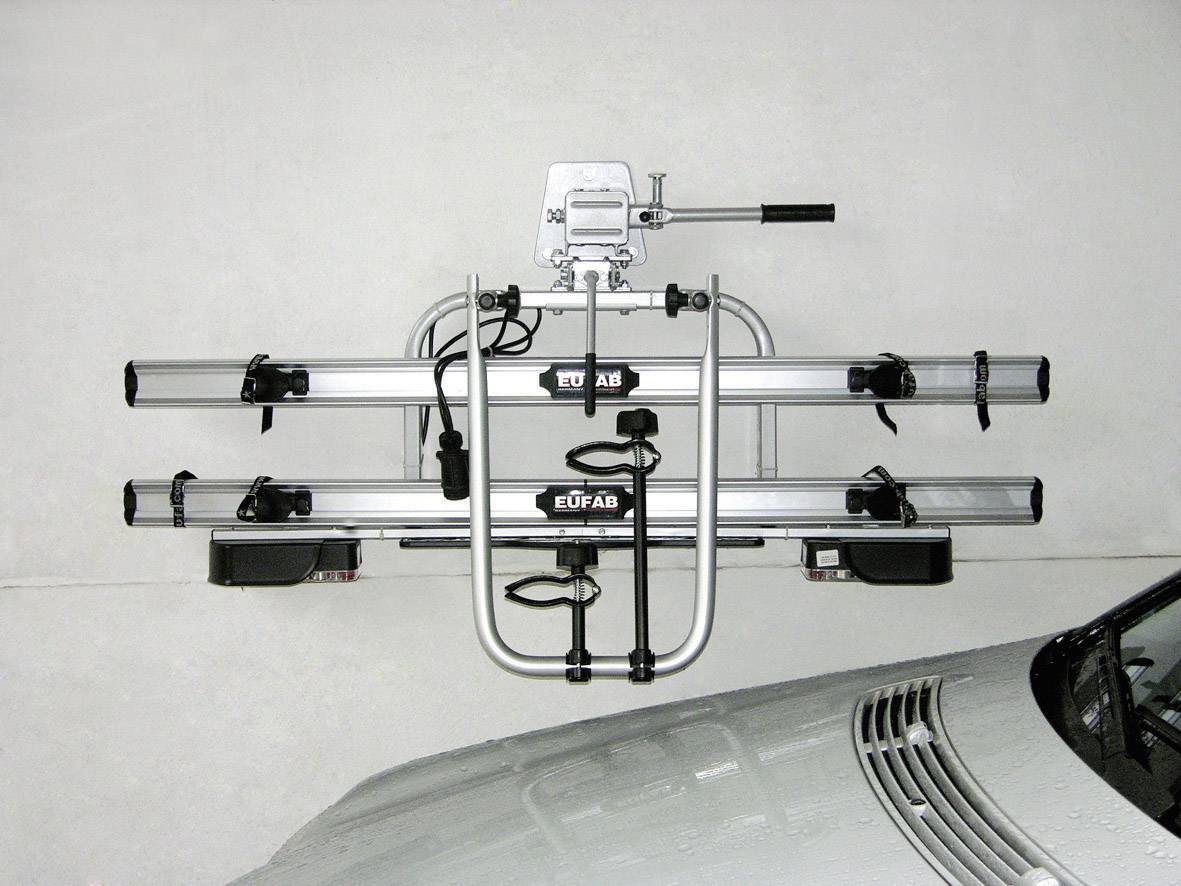Bicycle carrier mounted on a white wall next to a silver vehicle. The carrier is ready for bicycle attachment.