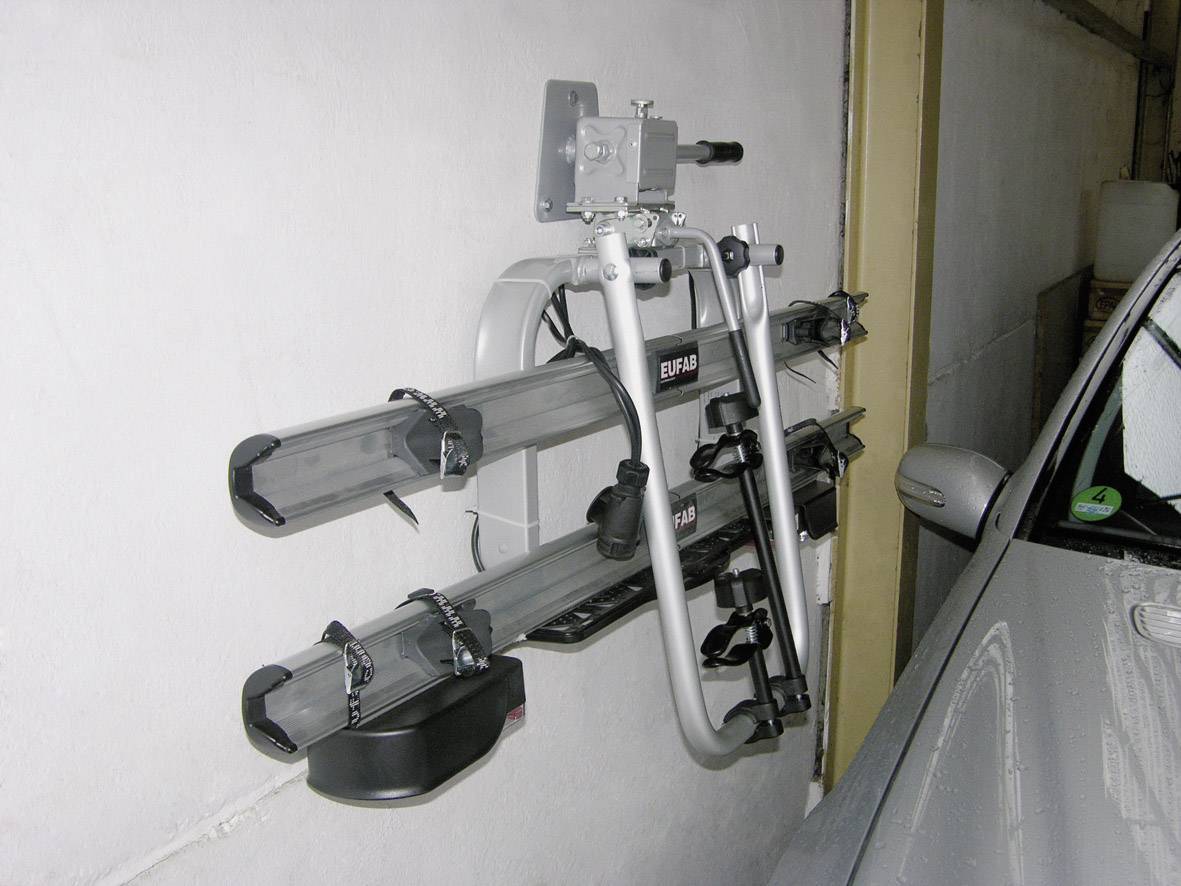 A folded bicycle rack is mounted on a wall in a garage, next to a parked car.