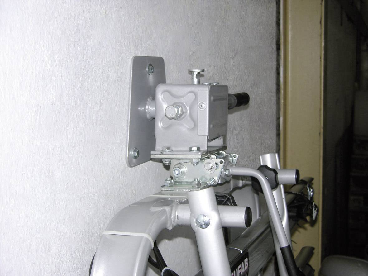 A metal padlock with a chain secures a folded garden tool to a wall bracket.