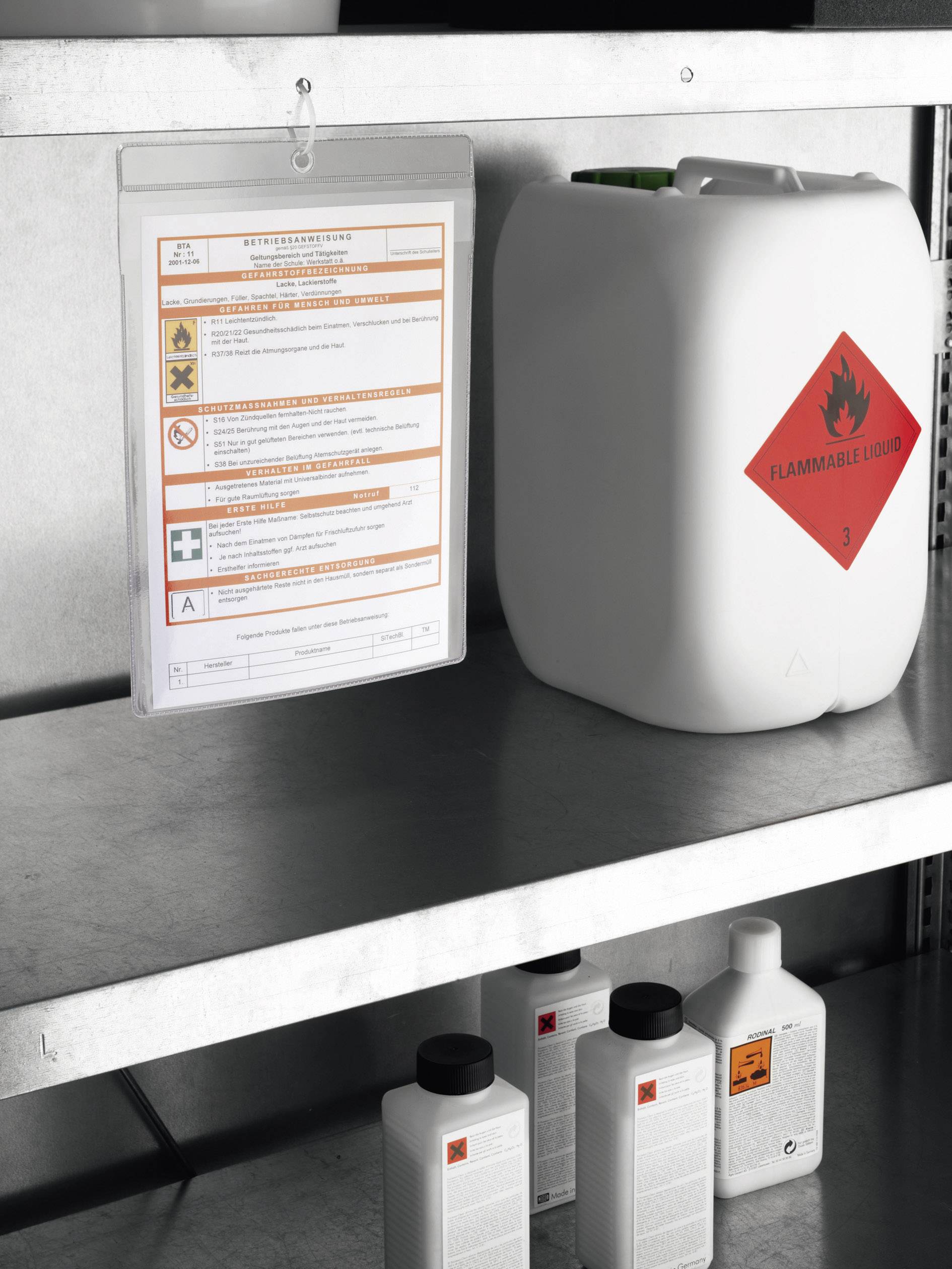 On a metal shelving unit stands a white canister with the label 'Flammable Liquid', alongside safety information and other containers.