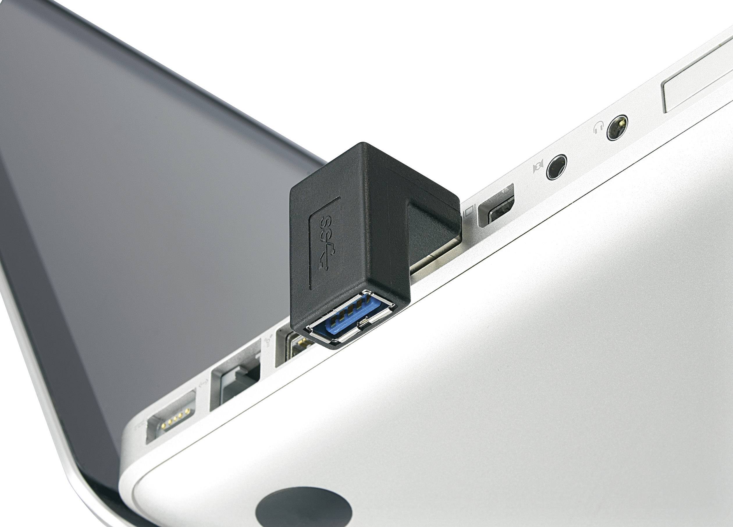 A black USB plug is inserted into the USB port of a silver laptop. The laptop is partially open.