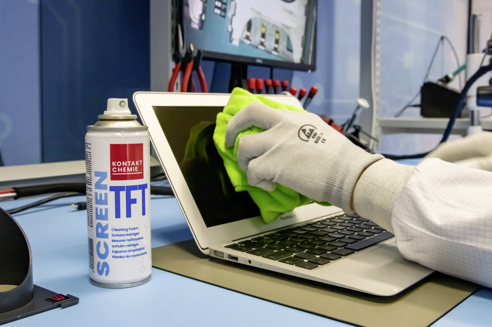 Une personne nettoie l'écran d'un ordinateur portable avec un chiffon vert et un produit de nettoyage pour écran dans un environnement technique.