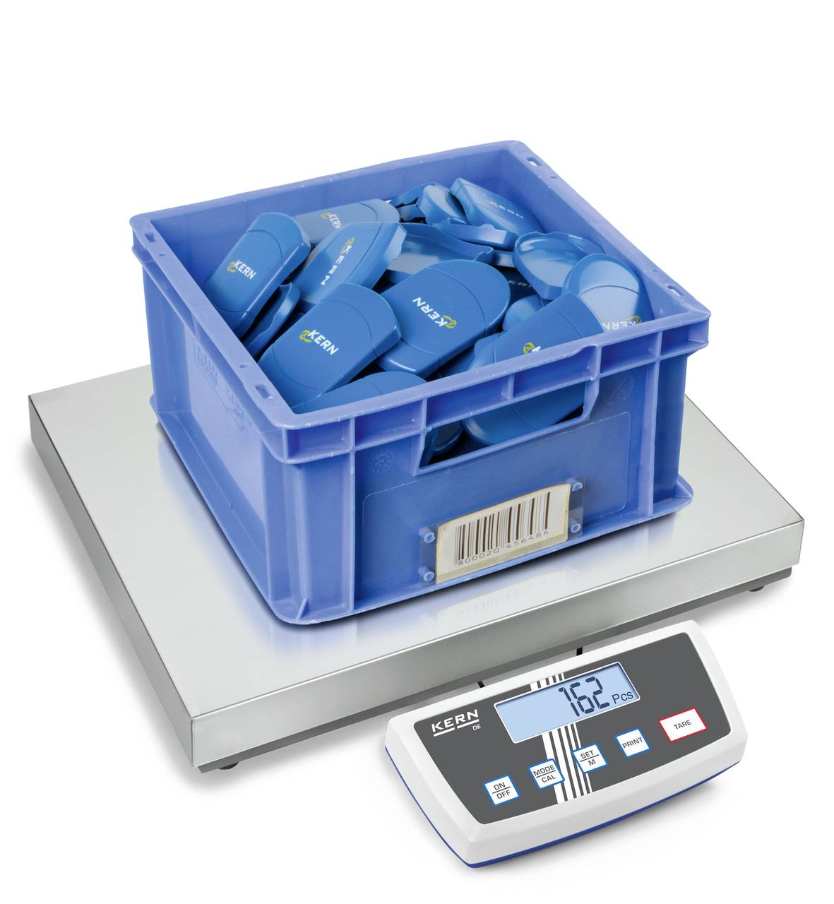 Une boîte bleue remplie de pièces en plastique bleu est posée sur une balance. L'affichage indique '1,62 kg'.