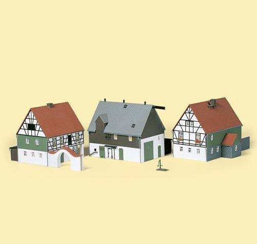Modèle de trois maisons de style traditionnel allemand avec des toits rouges et une ossature en bois, sur un fond uni.