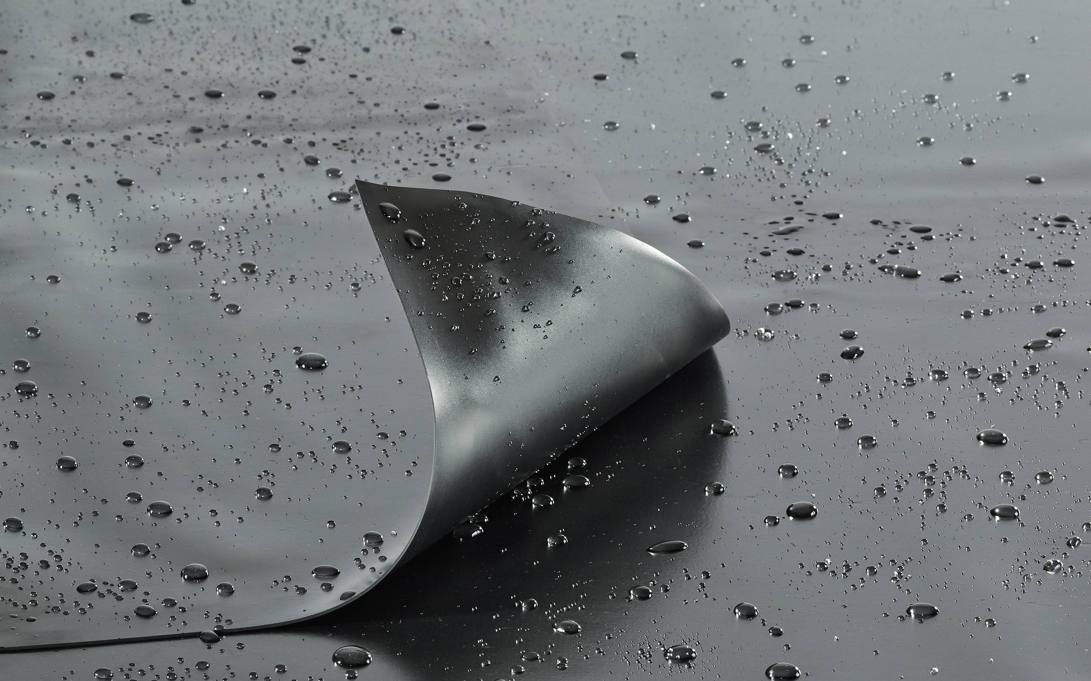 Un morceau de plastique sombre et recourbé repose sur une surface humide avec des gouttelettes d'eau dispersées, mettant en évidence sa nature hydrofuge.