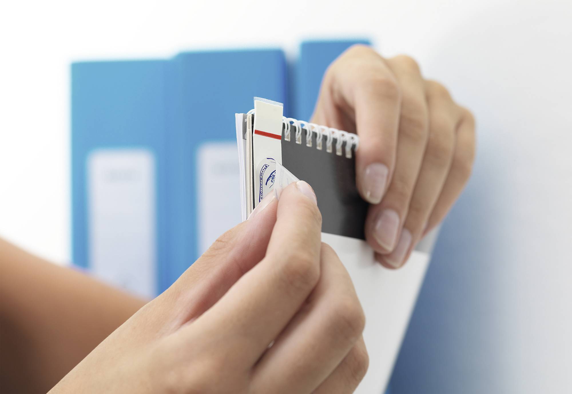 Plan rapproché de mains feuilletant un nuancier devant des classeurs bleus. Sélection de couleurs ou de matériaux.