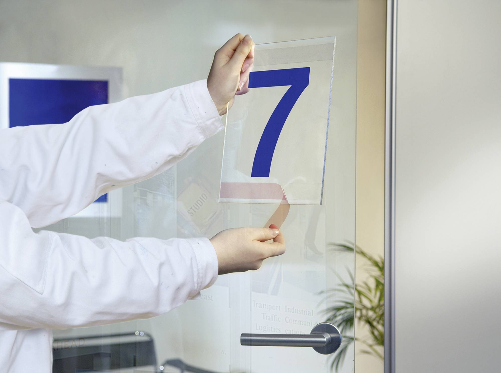 Une personne accroche un panneau de porte avec un grand numéro 7 bleu sur une porte vitrée.