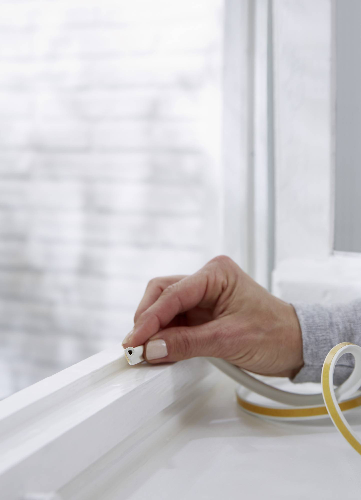 'Une main pose une bande de joint d'étanchéité sur un cadre de fenêtre afin d'améliorer l'isolation.'