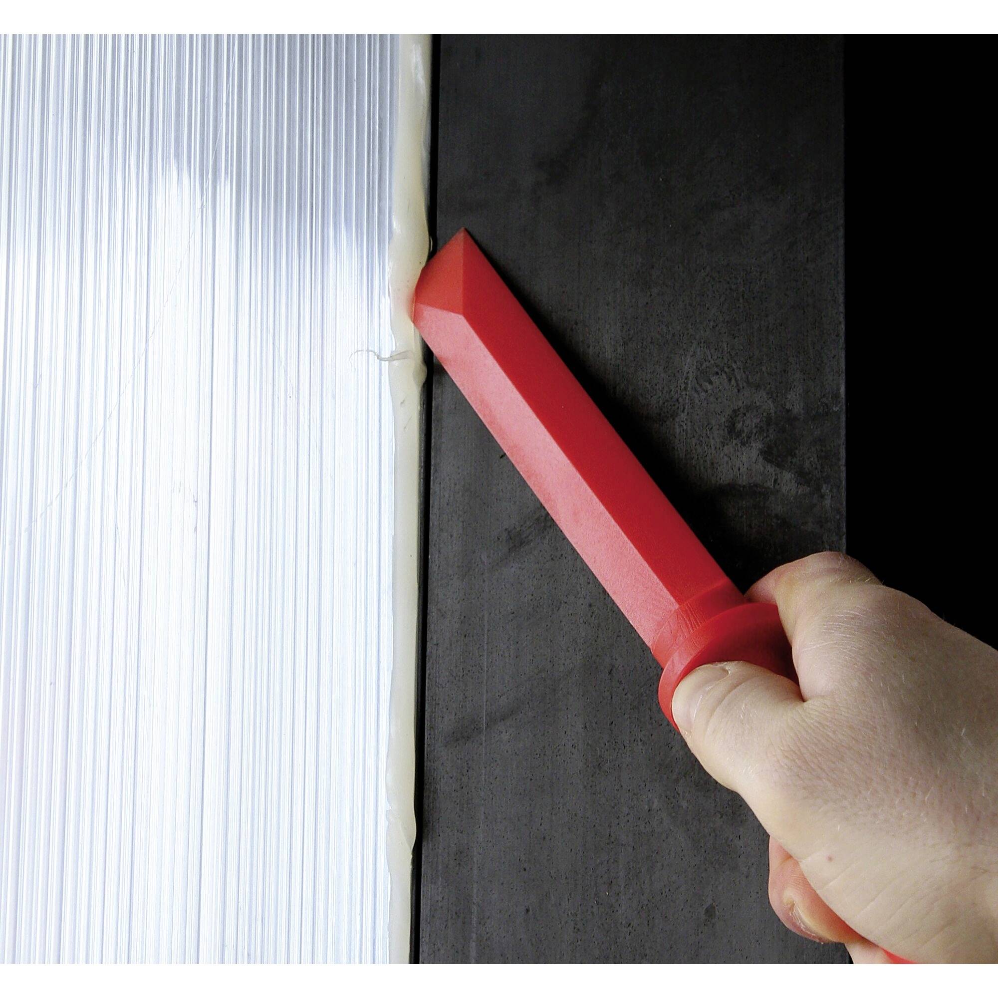 Une main tient un outil rouge qui trace une ligne blanche le long d'une surface noire, probablement pour couper.