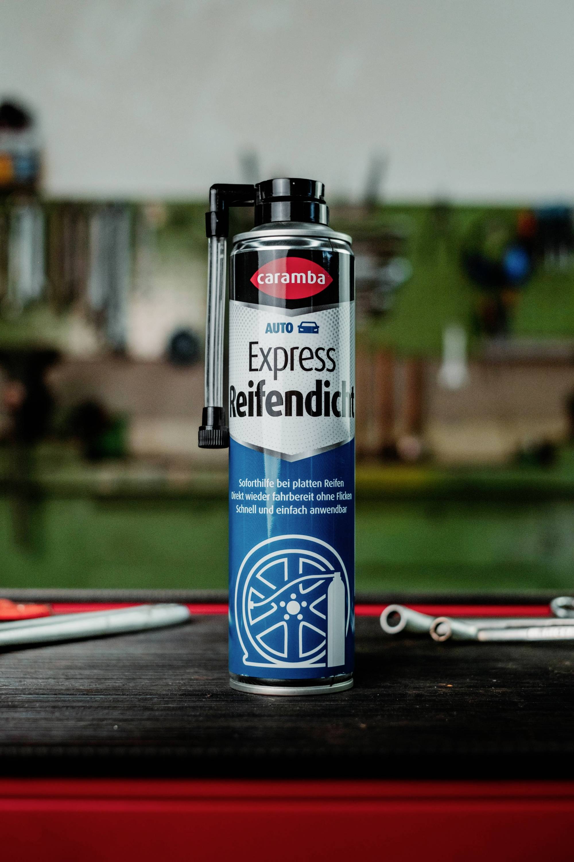 Une canette de produit d'étanchéité pour pneus 'Caramba Auto Express Reifendicht' sur un établi, avec des outils d'atelier flous en arrière-plan.