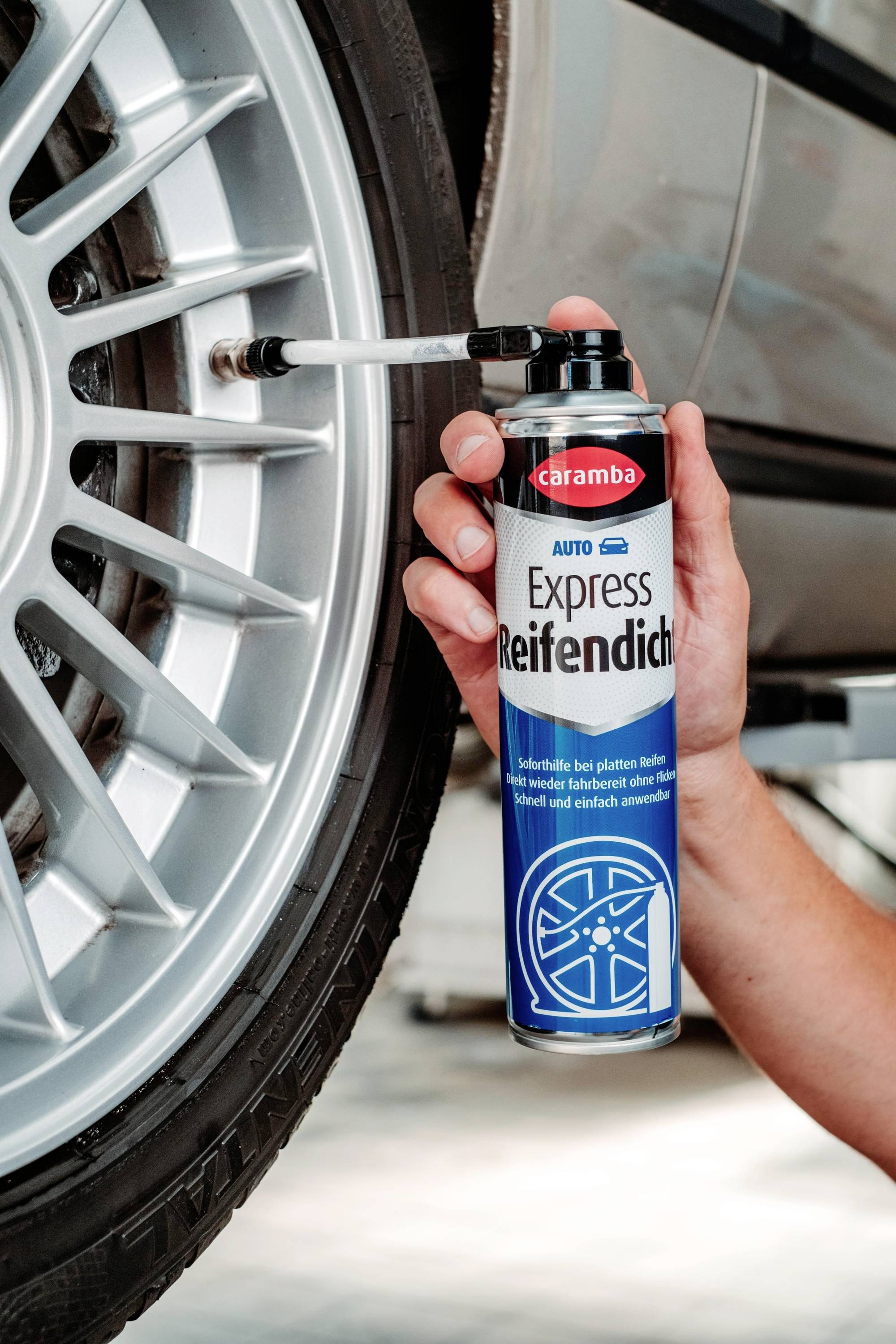 Une personne tient une bombe aérosol étiquetée « Express Reifendicht » près d'un pneu de voiture, l'utilisant pour appliquer un produit d'étanchéité sur la jante.