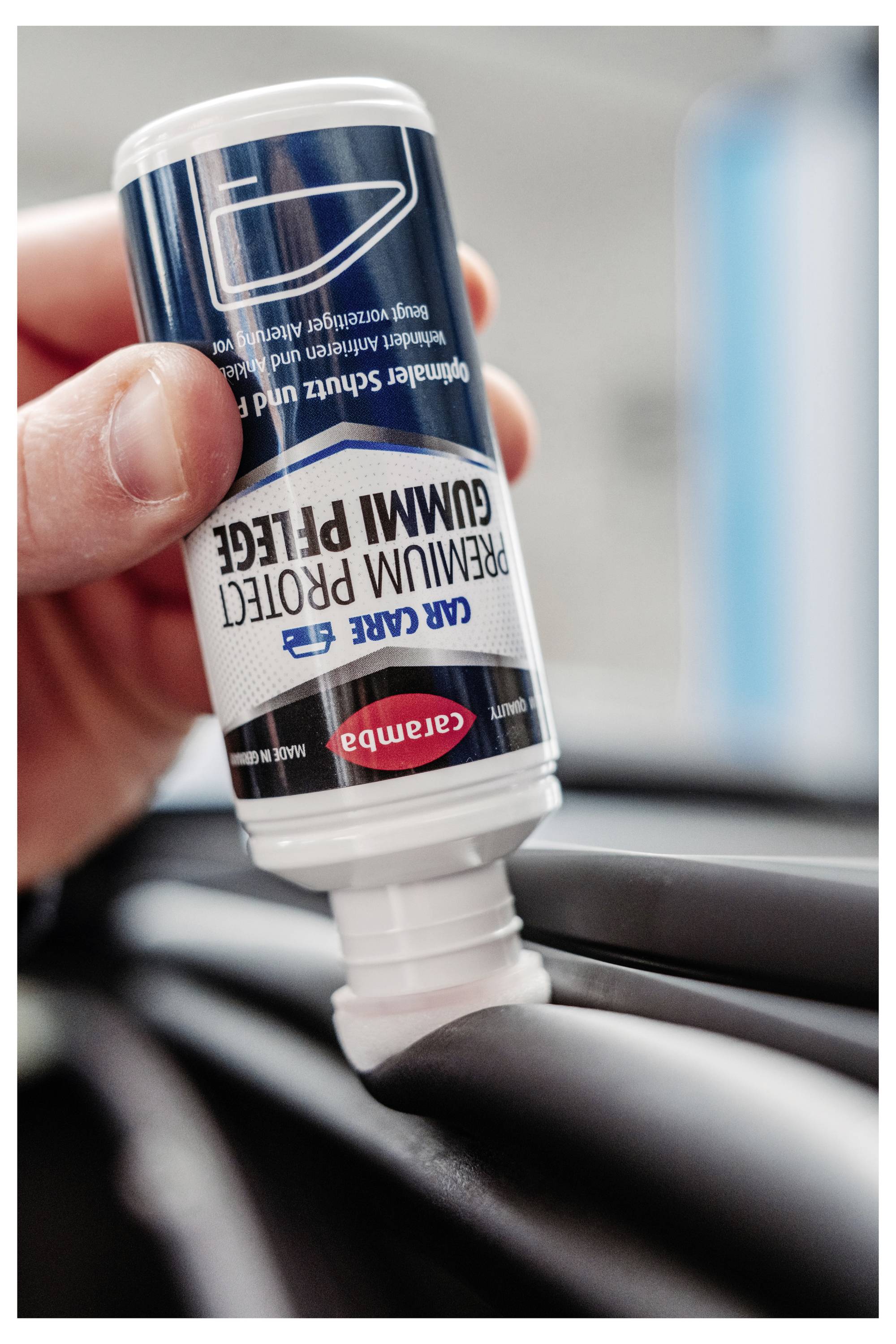 Main tenant une bouteille inversée de crème CARE GUMM PROTECT tout en l'appliquant sur un pneu de voiture noir ou un garniture.