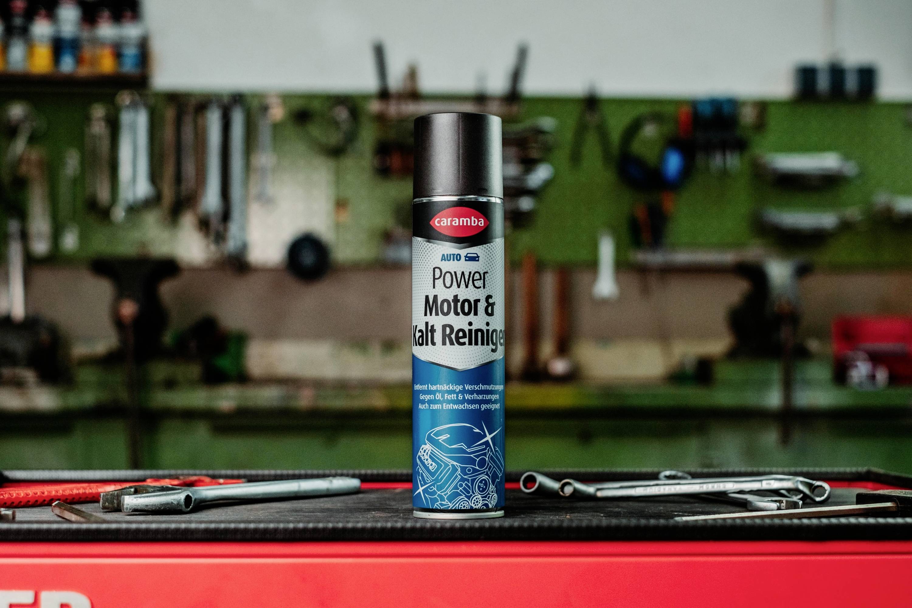 Une canette de produit nettoyant moteur 'Caramba Power Motor & Kalt Reiniger' est centrée sur un établi, avec des outils en arrière-plan flou et un environnement d'atelier.