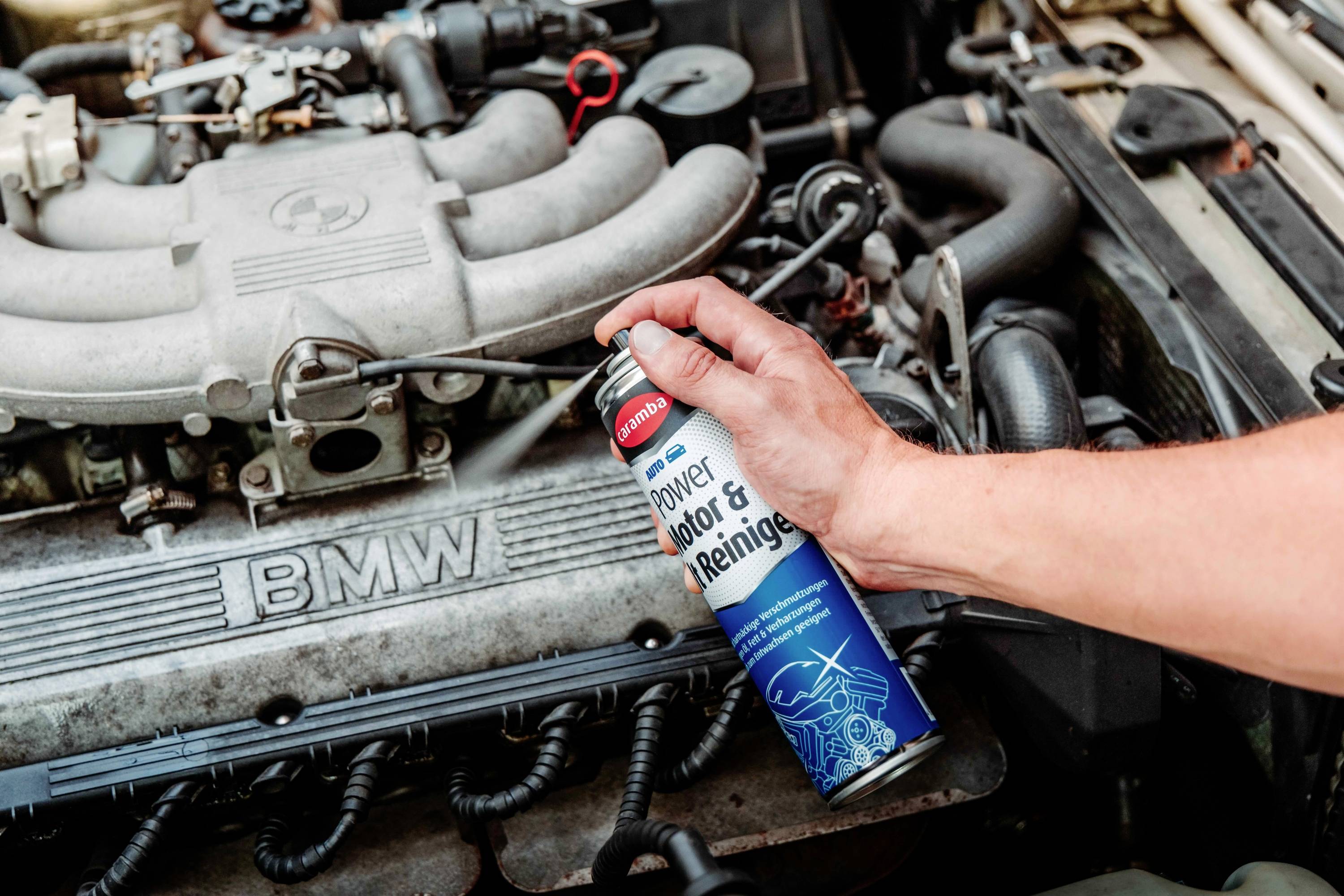 Un manuel pulvérise du « Power Motor & Engine Cleaner » sur un moteur BMW ouvert, indiquant l'entretien ou le nettoyage des composants du moteur.