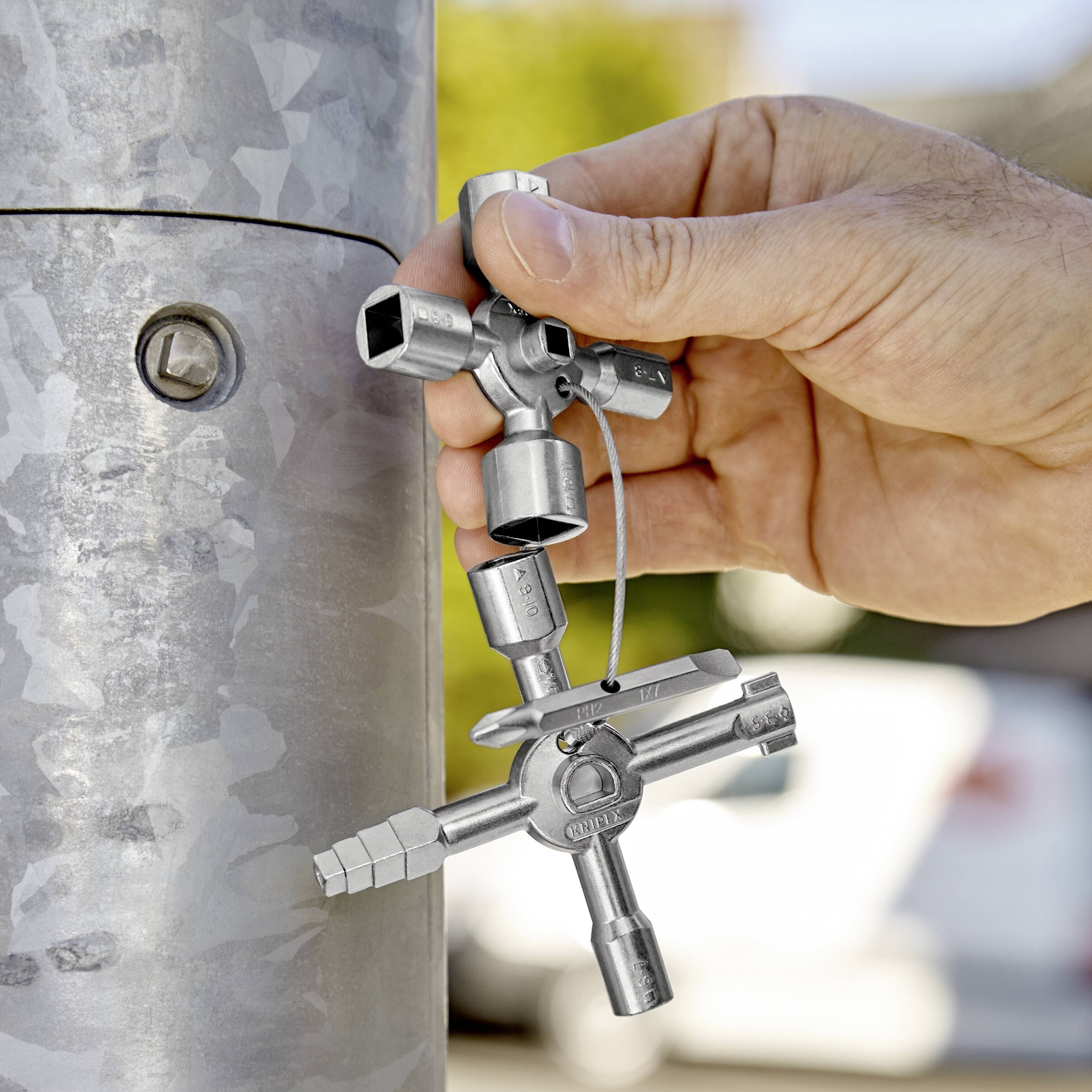 Une main tient une clé à quatre pans près d'une surface métallique. La clé possède plusieurs embouts et semble polyvalente.