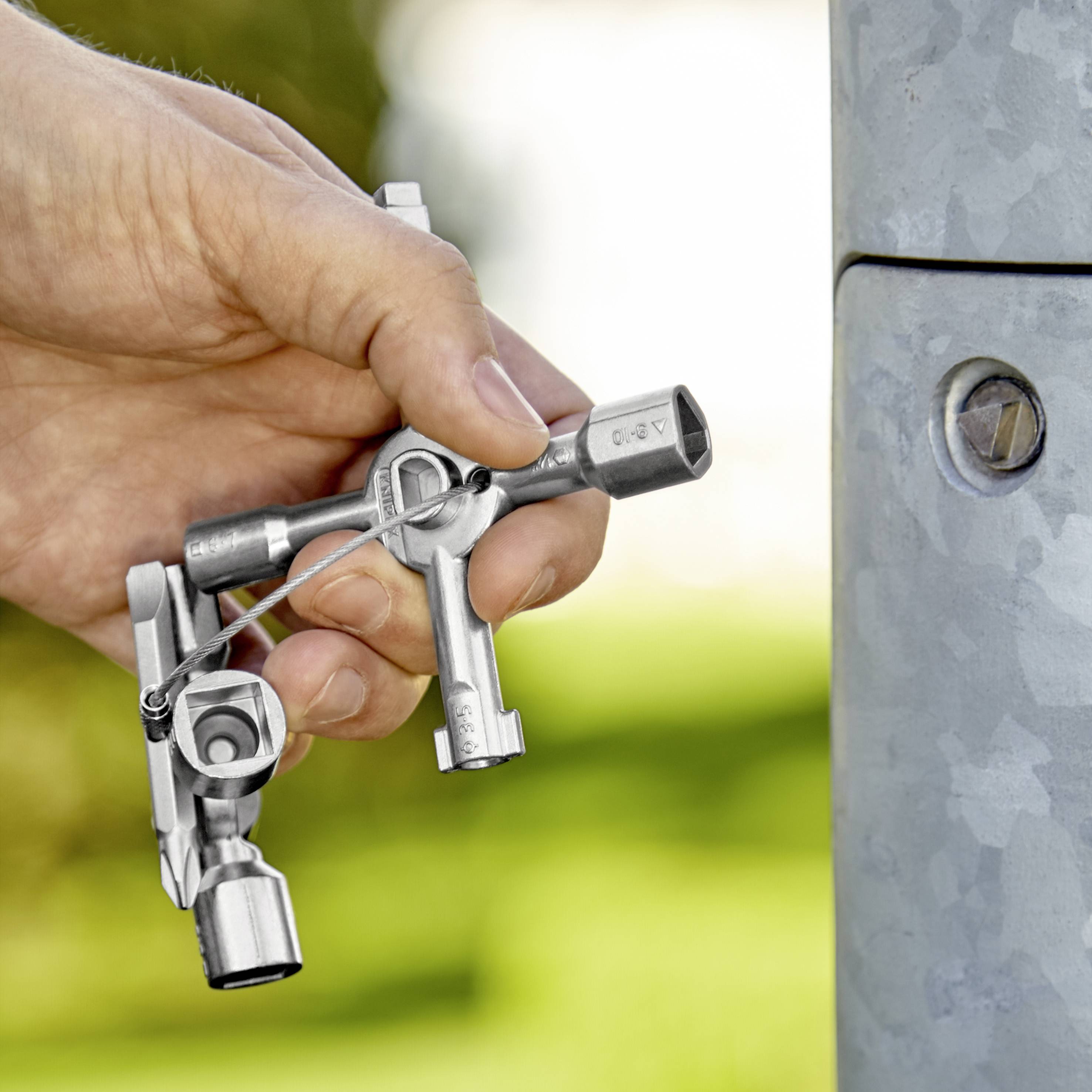 Une main tient une clé allen pour desserrer ou resserrer un boulon sur un poteau métallique, à l'extérieur.