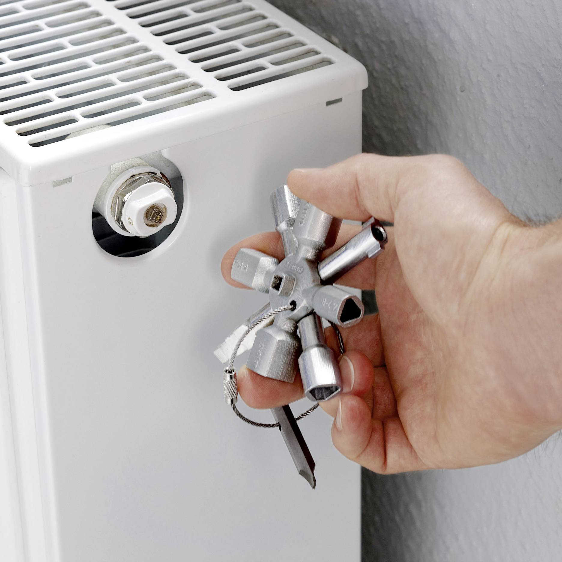 Une personne purge un radiateur à l'aide d'une clé de purge.