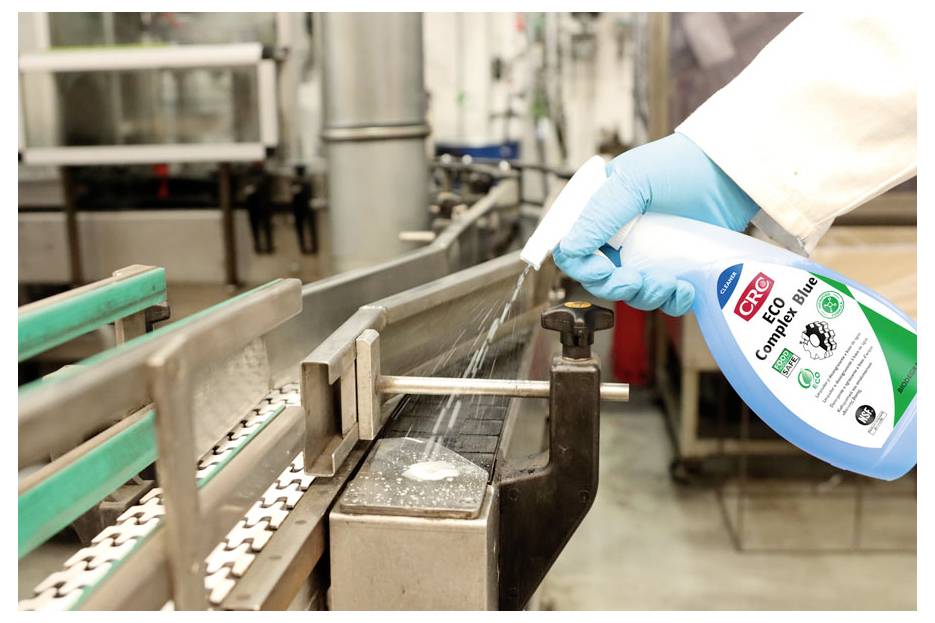 Une personne portant des gants bleus vaporise du 'Nettoyant de Contact CRC' sur un tapis roulant dans un environnement industriel, ce qui indique une opération de maintenance ou de nettoyage.