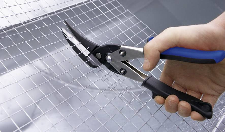 Une main coupe une grille métallique avec des cisailles.