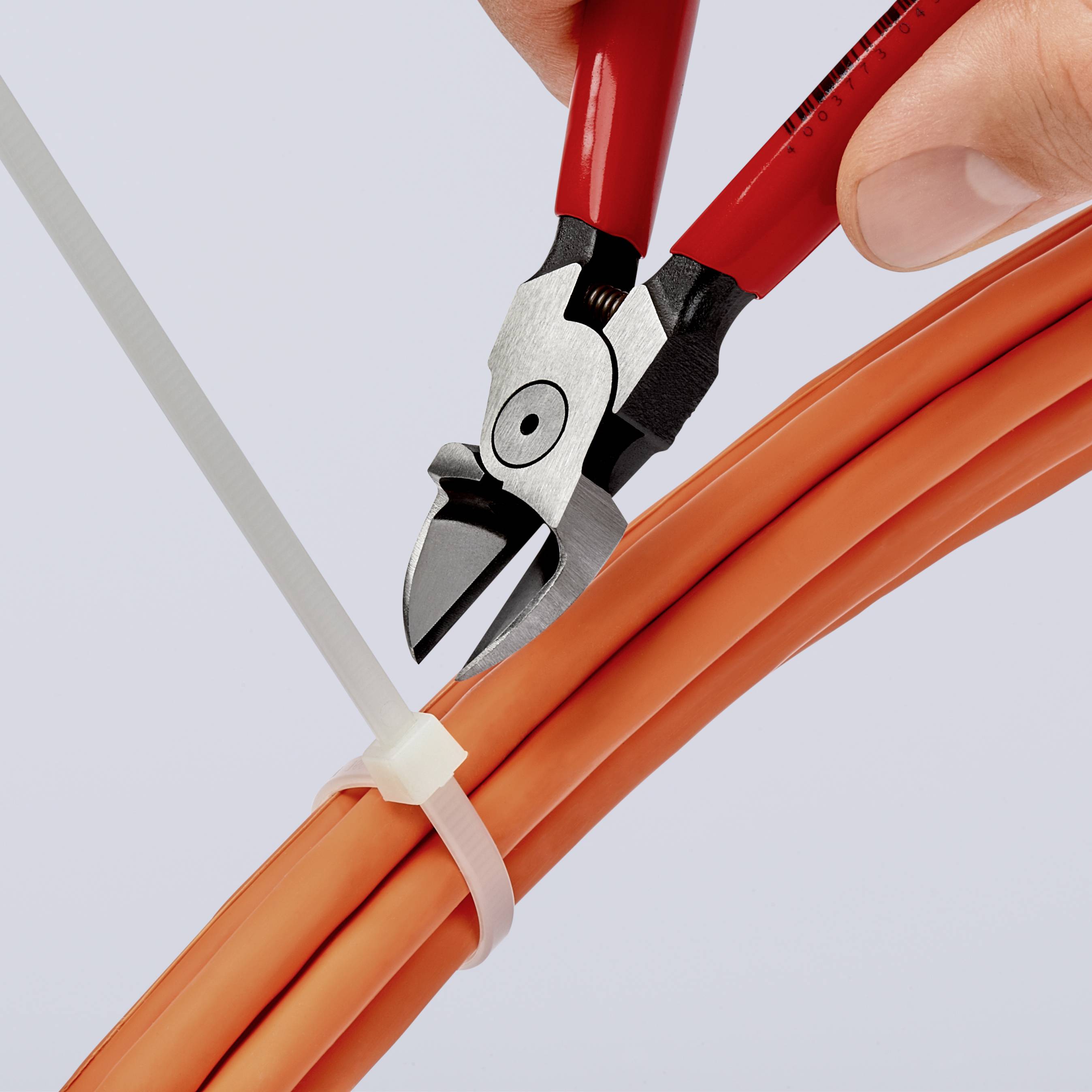 Une main coupe un collier de serrage blanc avec une pince rouge, qui est enroulé autour de plusieurs câbles orange.