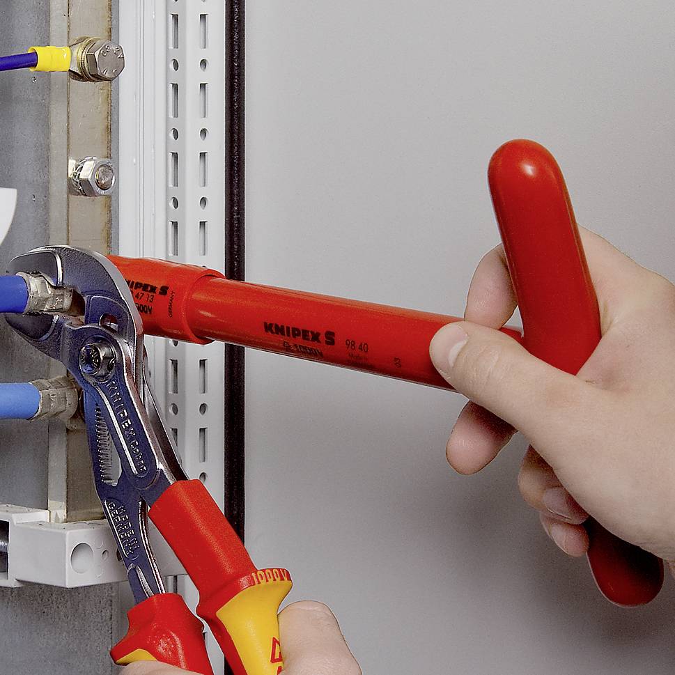 Une personne utilise deux outils, dont une pince, pour fixer des câbles dans un tableau électrique.