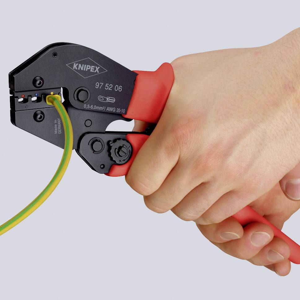 Une main tient une pince à sertir rouge et travaille un câble vert et jaune. La pince est de la marque Knipex.