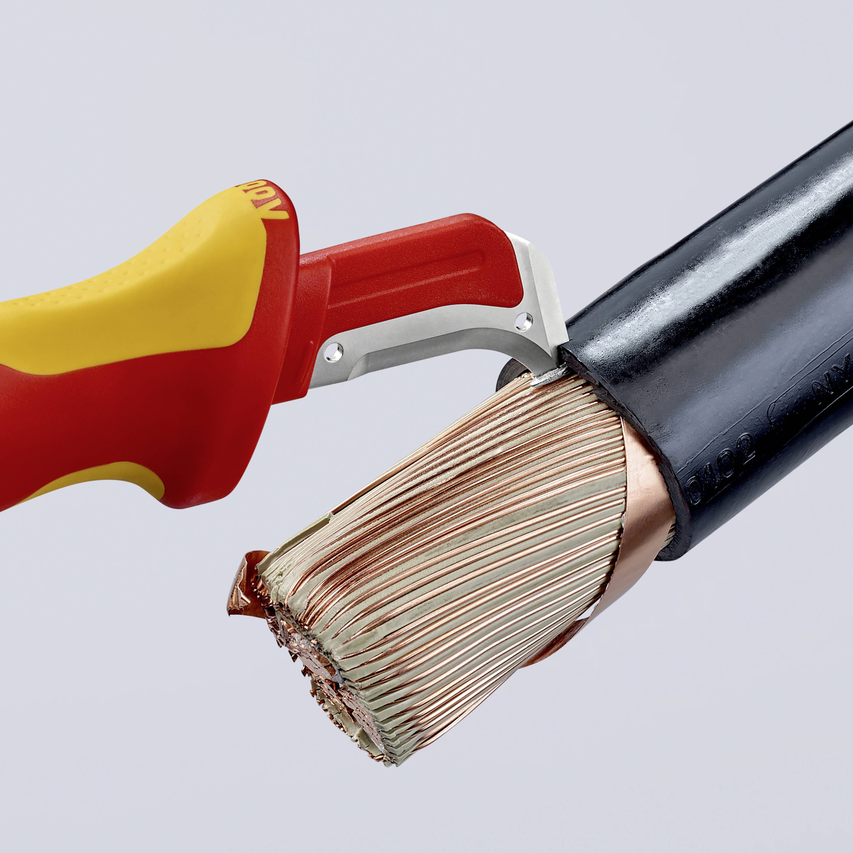 Un dénudeur retire l'isolation d'un câble électrique, montrant les fils de cuivre mis à nu. L'outil est rouge et jaune.