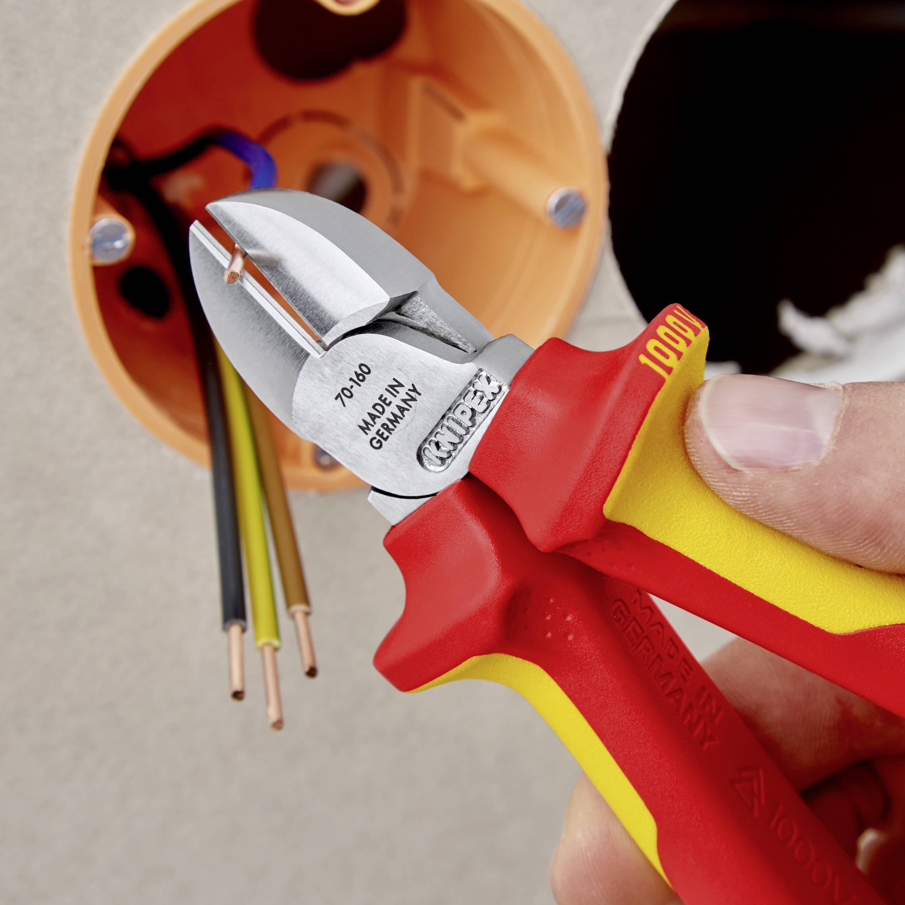 Une main tient un coupe-câbles isolé à côté de fils électriques, prête à couper. Outils pour travaux électriques.
