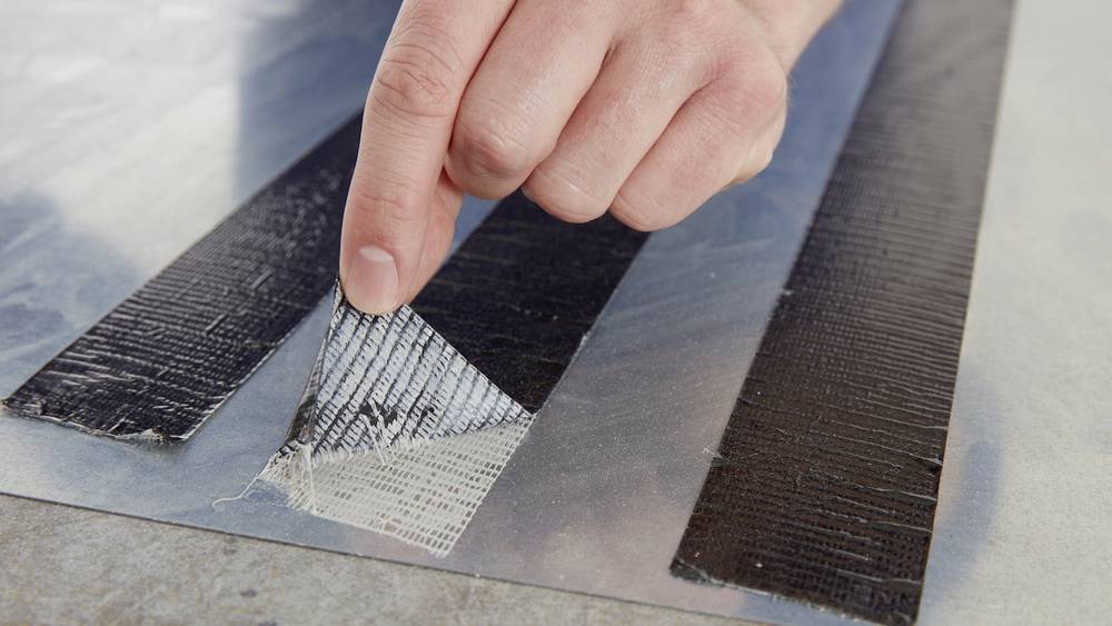 Une main retire du ruban adhésif d'une surface métallique, révélant une section brillante et réfléchissante.