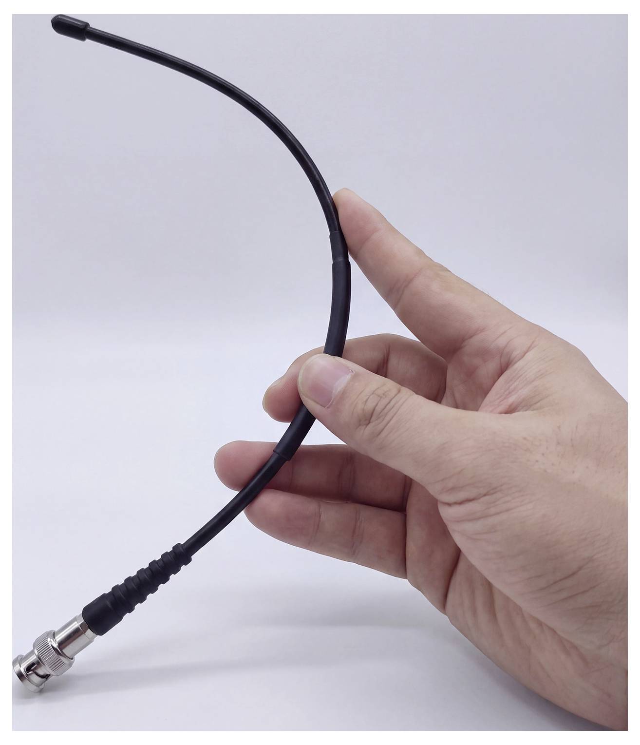 Main tenant un câble coaxial noir avec un connecteur métallique, montré sur un fond blanc uni.