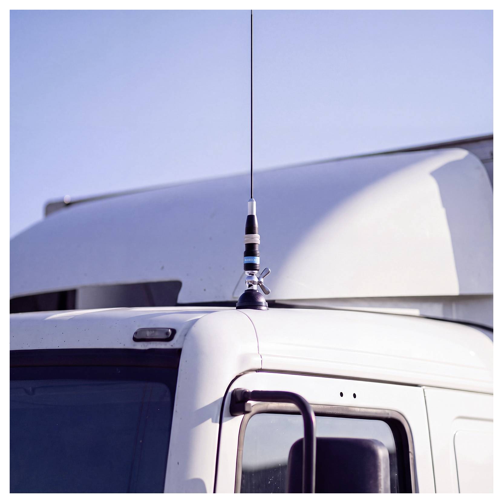 Gros plan d'une cabine de camion blanc avec une antenne verticale montée sur le toit sur fond de ciel dégagé.