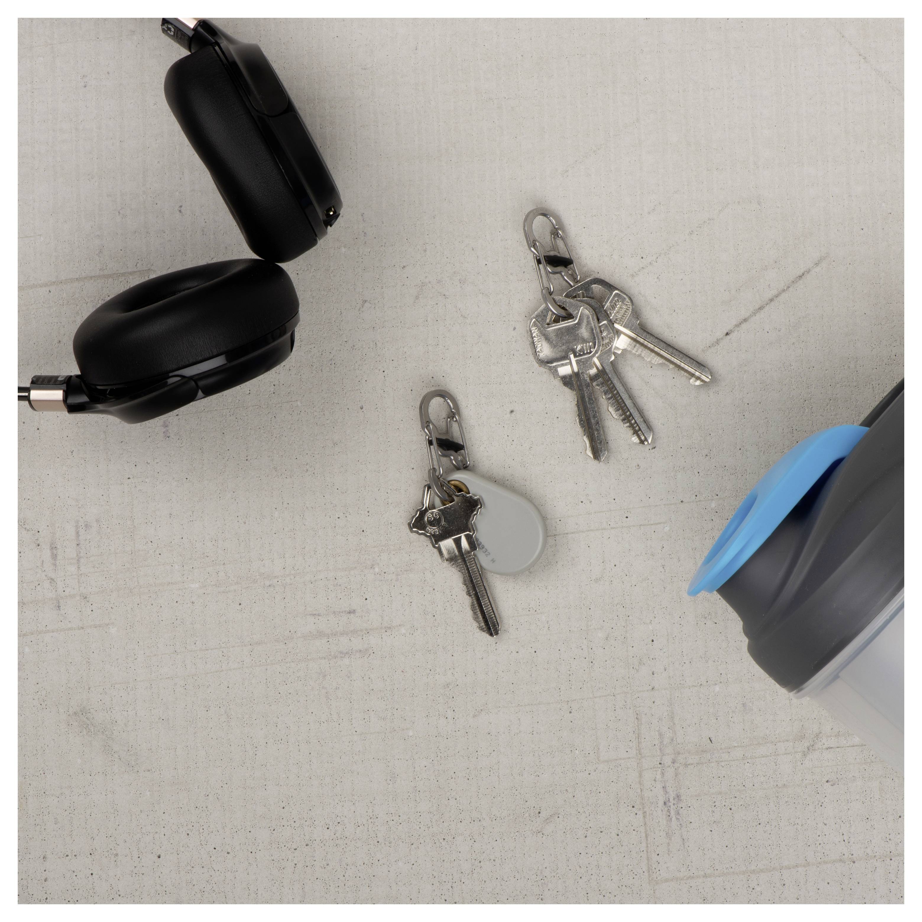Des écouteurs sans fil, un shaker, et deux jeux de clés sur une surface gris clair.