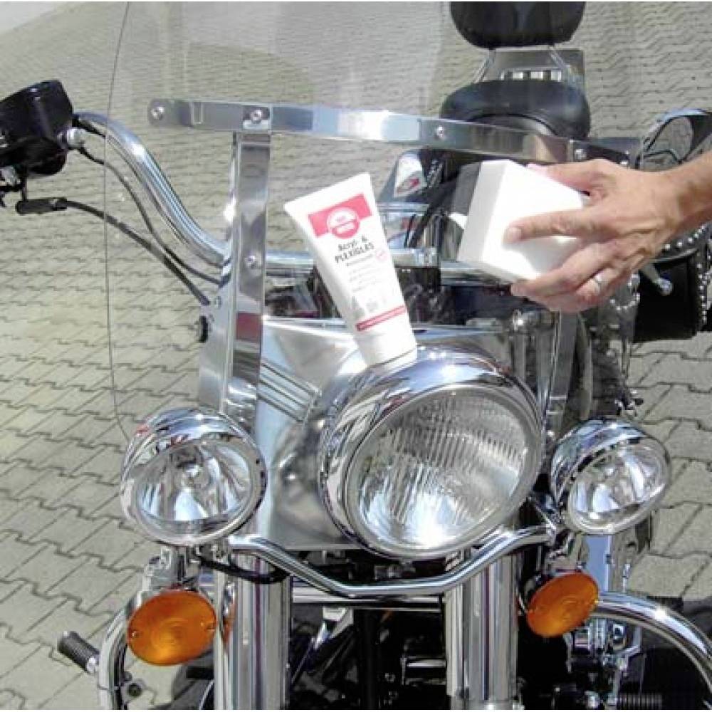 Une personne nettoie les parties chromées d'une motocyclette avec un chiffon et du polish, mettant en valeur l'entretien de l'extérieur du véhicule.