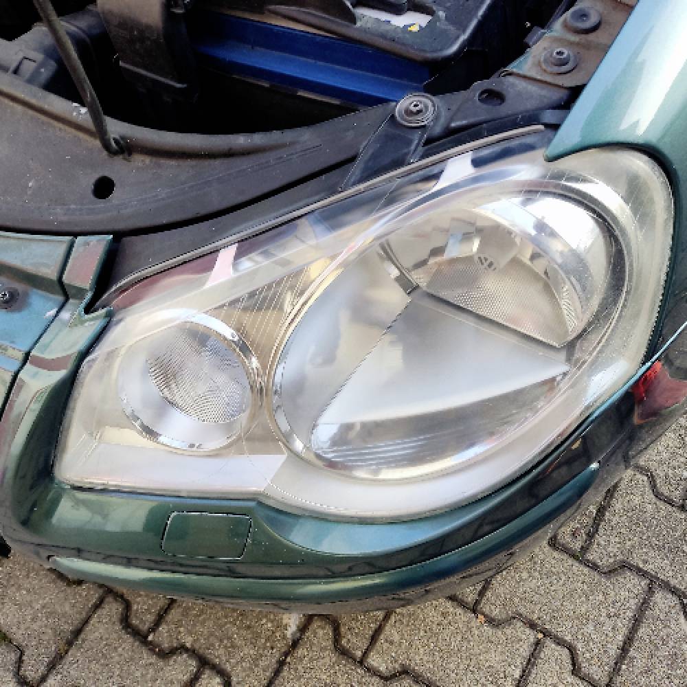 Gros plan sur le phare gauche d'une voiture verte et une partie de son pare-chocs, révélant les détails de conception du phare et son emplacement.