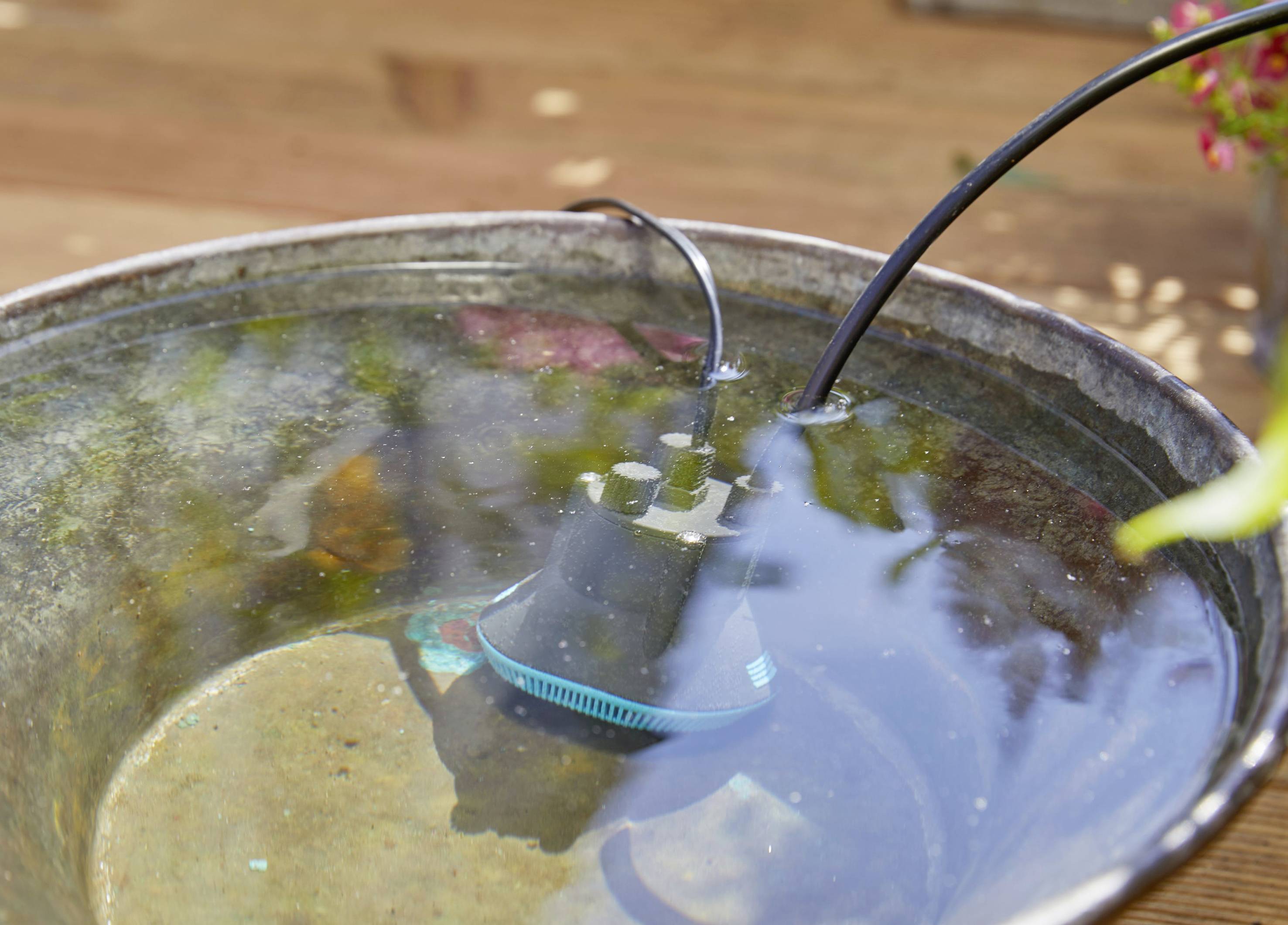 Un appareil électrique noir flotte partiellement dans un bol métallique rempli d'eau. Un câble sort de l'appareil.