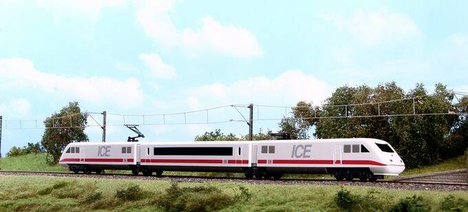Un train haute vitesse blanc et rouge se déplace sur une voie ferrée à travers un paysage herbeux sous un ciel bleu avec des nuages épars.