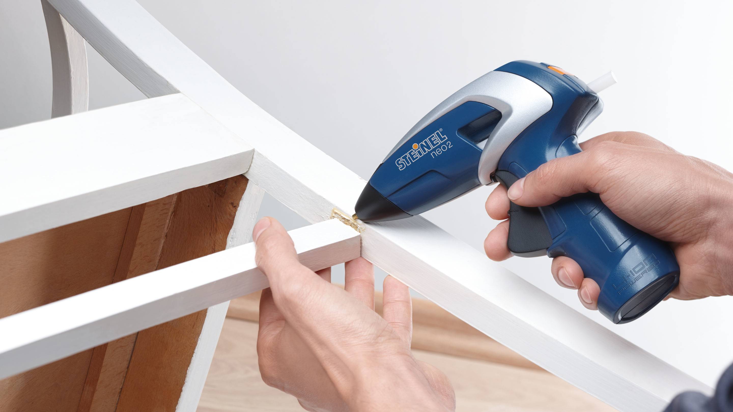 Une personne applique de la colle à l'aide d'un pistolet à colle bleu sur le bord d'un morceau de bois blanc pour le réparer.