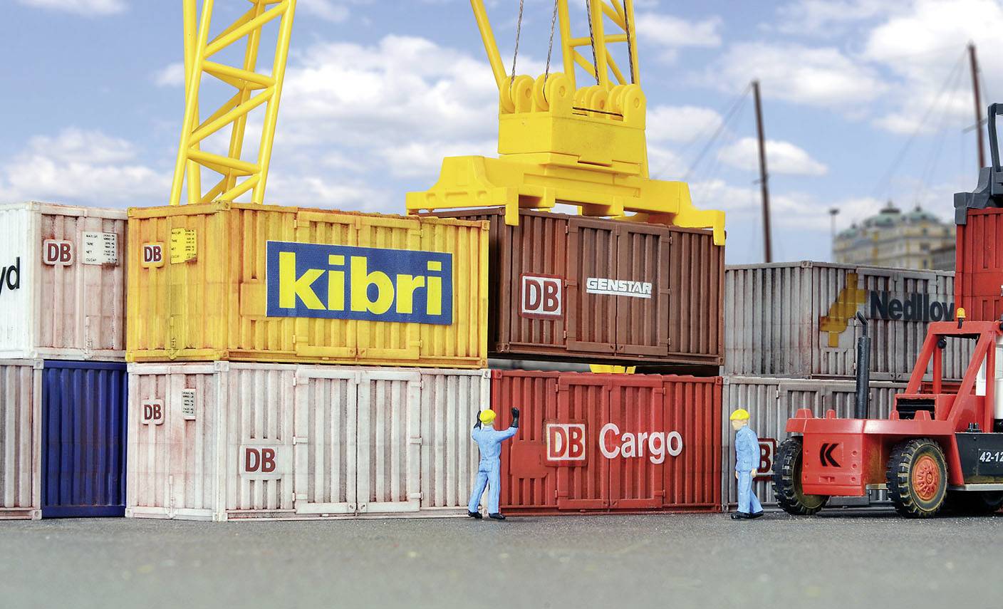 Deux ouvriers dans le port déplacent des conteneurs à l'aide d'une grue. Les conteneurs sont étiquetés 'DB Cargo' et 'kibri'. Un chariot élévateur est stationné à proximité.