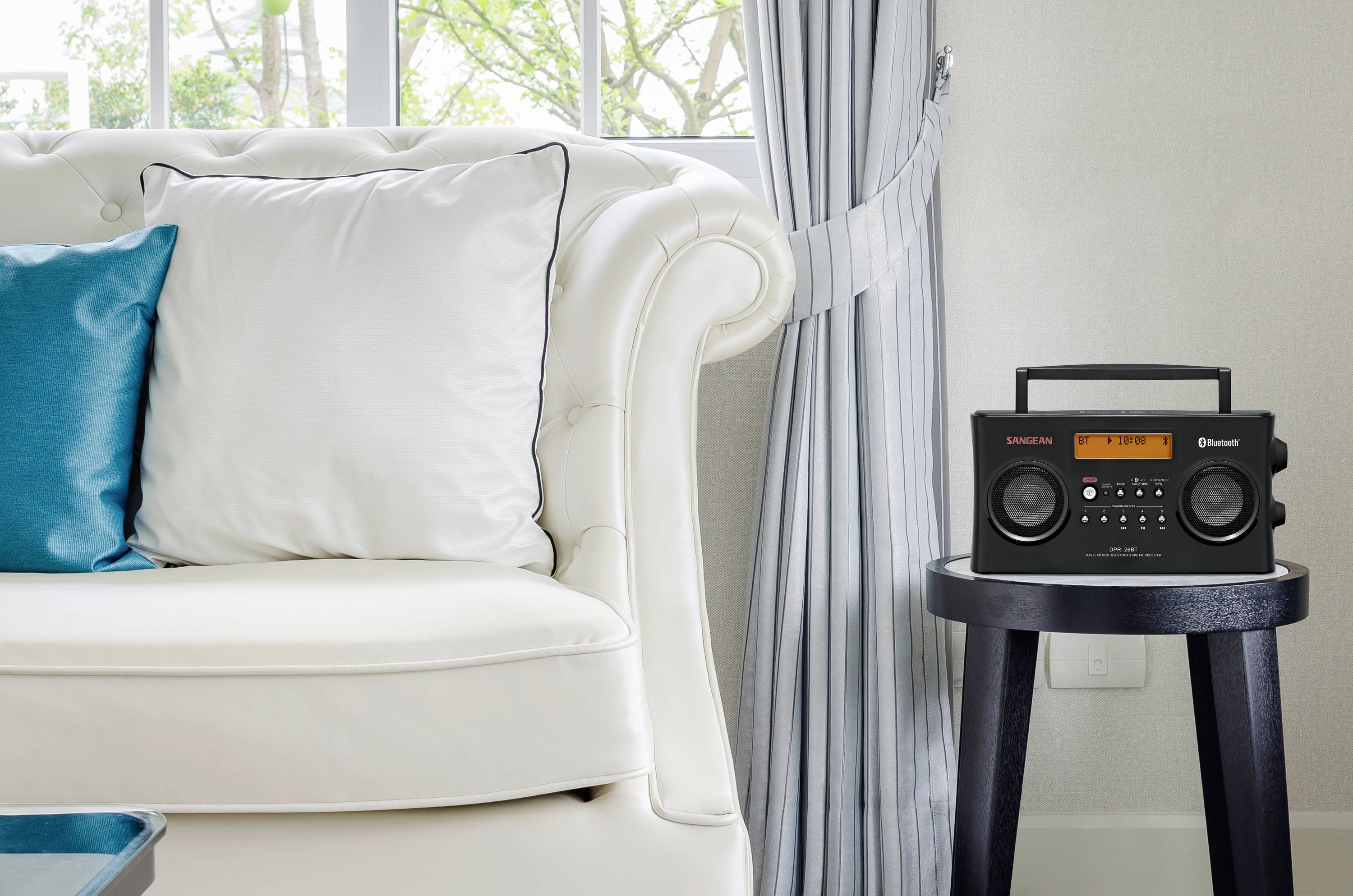 Un salon élégant avec un canapé blanc et un coussin bleu. À droite, sur une petite table, se trouve un poste de radio noir avec un affichage.